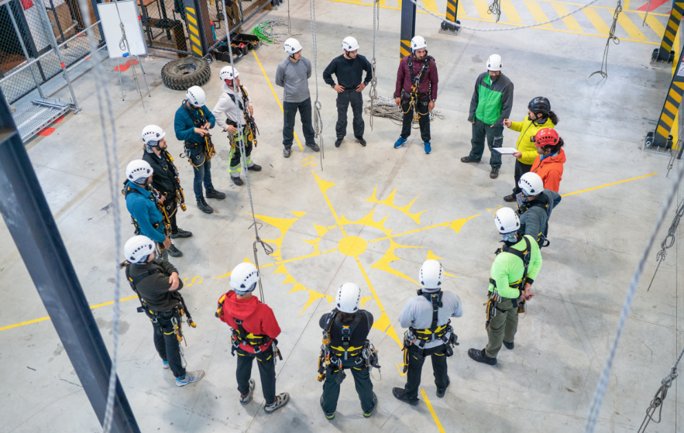 Windenergie-Techniker in Gurten und Helmen während einer Seilzugangstechnik-Schulung in einer Briefing-Runde