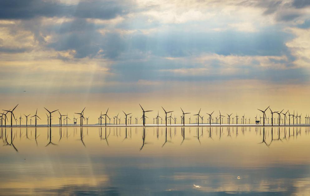 Offshore-Windpark bei Sonnenuntergang mit Turbinen, die sich im ruhigen Wasser spiegeln